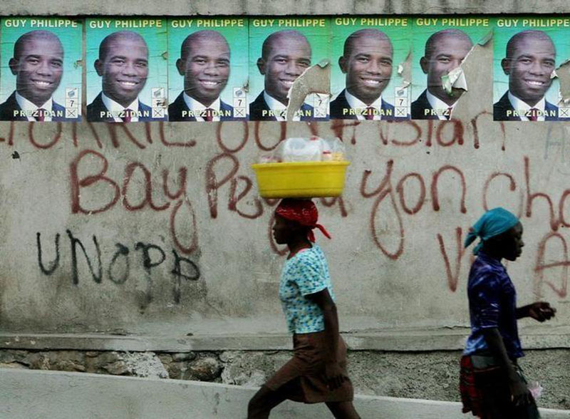 File - Haitians walk past posters of presidential candidate Guy Philippe at a street in Port-au-Prince, Haiti, on February 3, 2006. Photo: Reuters
