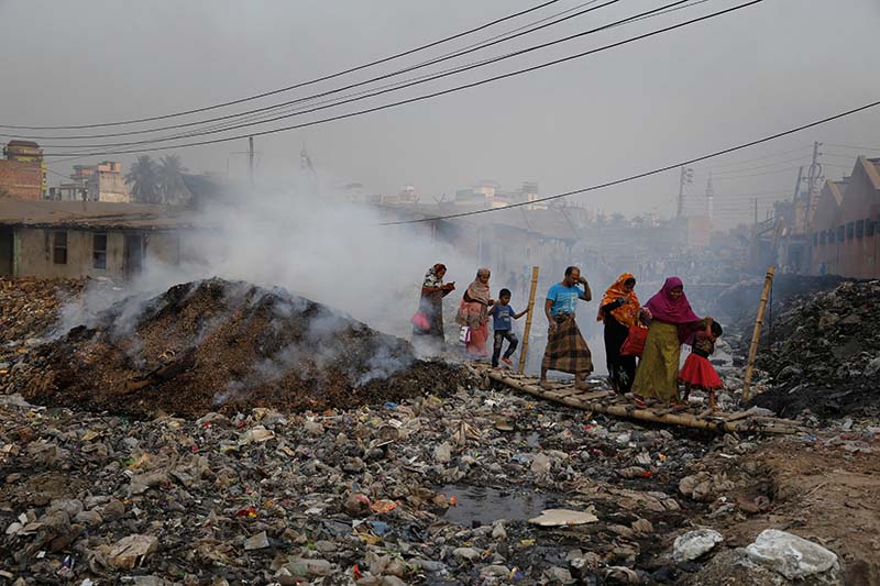 Bangladeshi people walk across a temporary bridge as smoke emits from tannery waste at the highly polluted Hazaribagh tannery area in Dhaka, Bangladesh, on Monday, February 6, 2017. Photo: AP