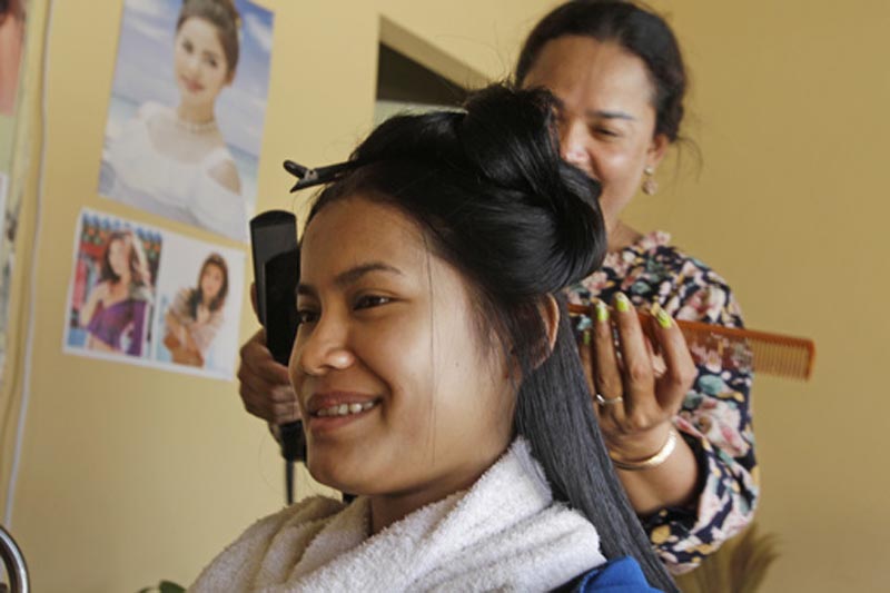 A customer smiles as she has her hair straightened during a break from her factory job on International Women's Day outside Phnom Penh, Cambodia, Wednesday, March 8, 2017. Photo: AP