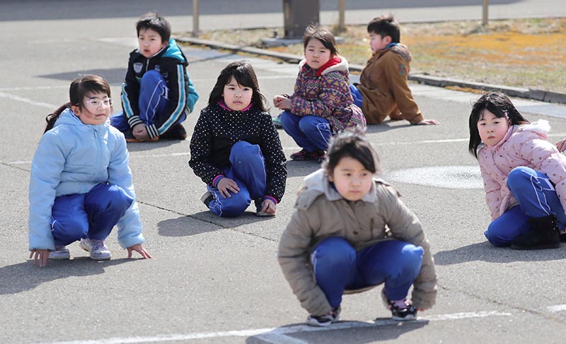 Elementary school students squat down on the street as they participate in an evacuation drill for local residents based on the scenario that a ballistic missile launched landed in Japanese waters, in Oga, Akita prefecture, Japan, on  March 17, 2017. Photo: Kyodo via Reuters