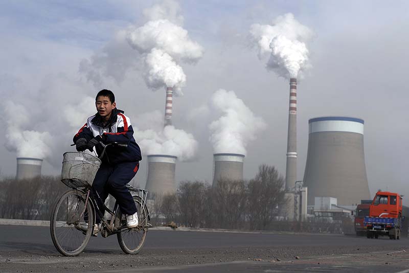 FILE - A Chinese boy cycles past cooling towers of a coal-fired power plant in Dadong, Shanxi province, China, on December 3, 2009. AP