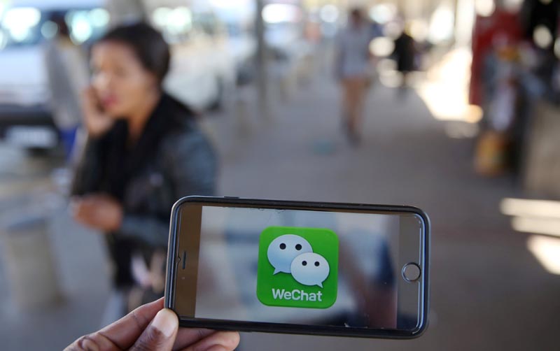 A WeChat logo is displayed on a mobile phone as a woman walks past as she talks on her mobile phone at a taxi rank in this picture illustration taken on July 21, 2016. Photo: Reuters