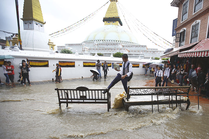A boy treads on benches to avoid stepping on to water-logged premises of Boudhanath Stupa after a spell of heavy rainfall, in Kathmandu, on Sunday, July 24, 2017. Photo: Skanda Gautam/THT