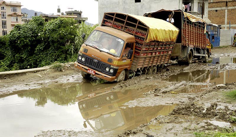 A labourer shifting crates of soft drinks to a bigger vehicle as a pick-up truck gets stuck in the middle of a muddy road, in Balkumari, on Monday, July 24, 2017. Photo: RSS