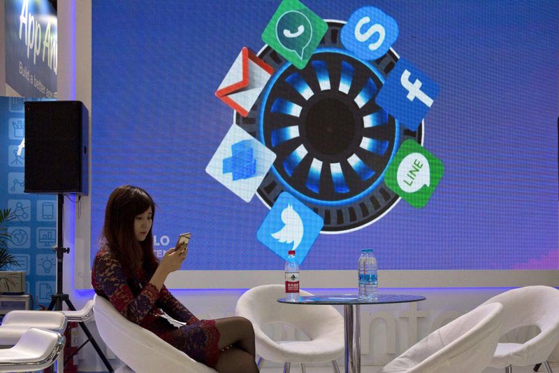 A woman browses her smartphone near icons depicting apps that are mostly banned in China during the Global Mobile Internet Conference in Beijing, on April 29, 2016. Photo: AP/ File