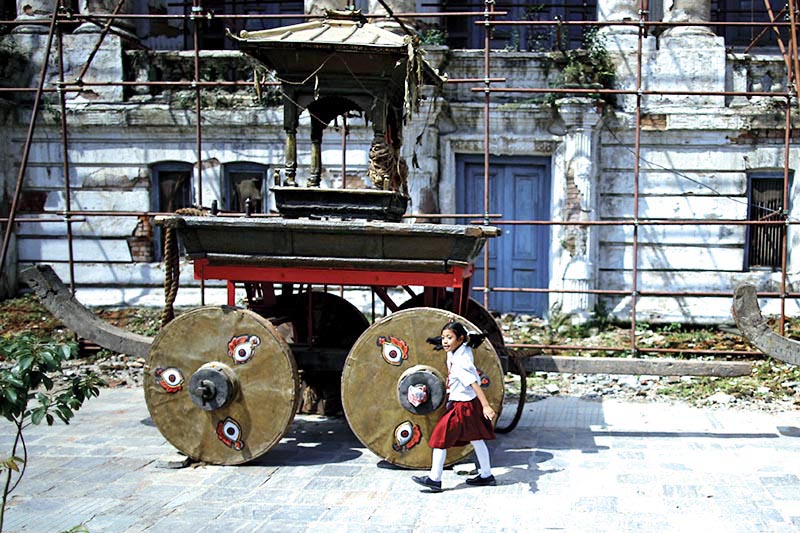 A schoolgirl passing by the wheels of a chariot built for the upcoming Indra Jatra festival, in Basantapur, Kathmandu, on Friday, September 01, 2017.