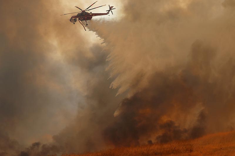 A helicopter drops water on a wind driven wildfire in Orange, California, US, on October 9, 2017. Photo: Reuters
