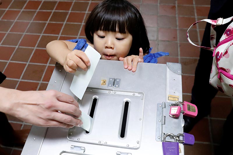 A girl casts her father's ballot for a national election at a polling station in Tokyo, Japan, on October 22, 2017. Photo: Reuters