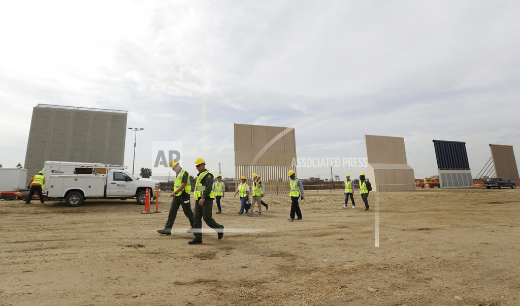 People pass border wall prototypes as they stand near the border with Tijuana, Mexico, Thursday, Oct. 19, 2017, in San Diego. Companies are nearing an Oct. 26 deadline to finish building eight prototypes of President Donald Trump's proposed border wall with Mexico. (AP Photo/Gregory Bull)