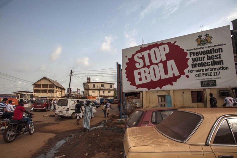 People pass a banner reading u2018STOP EBOLAu2019 forming part of Sierra Leoneu2019s Ebola free campaign in the city of Freetown, Sierra Leone, on Friday, January 15, 2016. Photo: AP/ File