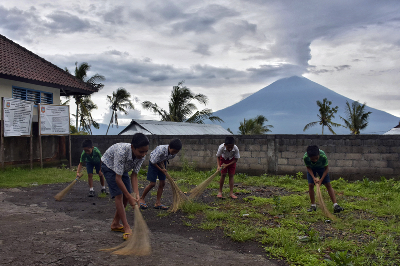 Students clean their schoolyard as Mount Agung is seen in the background in Bunutan, Bali, Indonesia, Thursday, November 30, 2017. Photo: AP