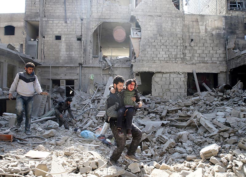 A man carries an injured boy as he walks on rubble of damaged buildings in the rebel held besieged town of Hamouriyeh, eastern Ghouta, near Damascus, Syria, on February 21, 2018. Photo: Reuters