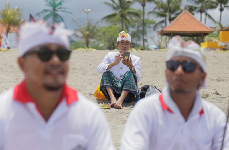A Balinese Hindu uses his mobile phone on a beach during a Melasti purification ceremony, ahead of the holy day Nyepi, in Gianyar, Bali, Indonesia March 14, 2018. Photo: Reuters 