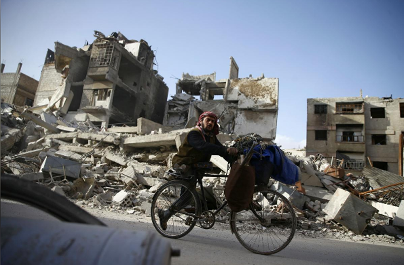 A handicapped man rides a bicycle past damaged buildings in the besieged town of Douma in eastern Ghouta in Damascus, Syria, March 1, 2018. Photo: Reuters 