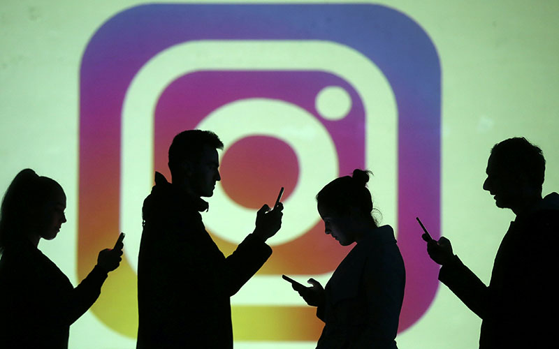 Silhouettes of mobile users are seen next to a screen projection of Instagram logo in this picture illustration taken on March 28, 2018. Photo: Reuters