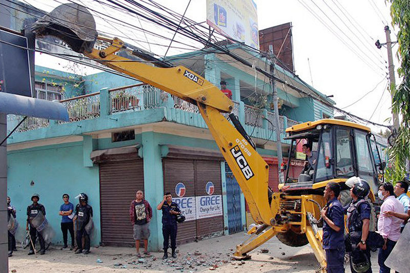 Locals along with security personnel observes as excavator demolishes illegally constructed structures along Butwal-Behaliya road section, in Rupandehi district, on Tuesday, April 17, 2018. Photo: RSS