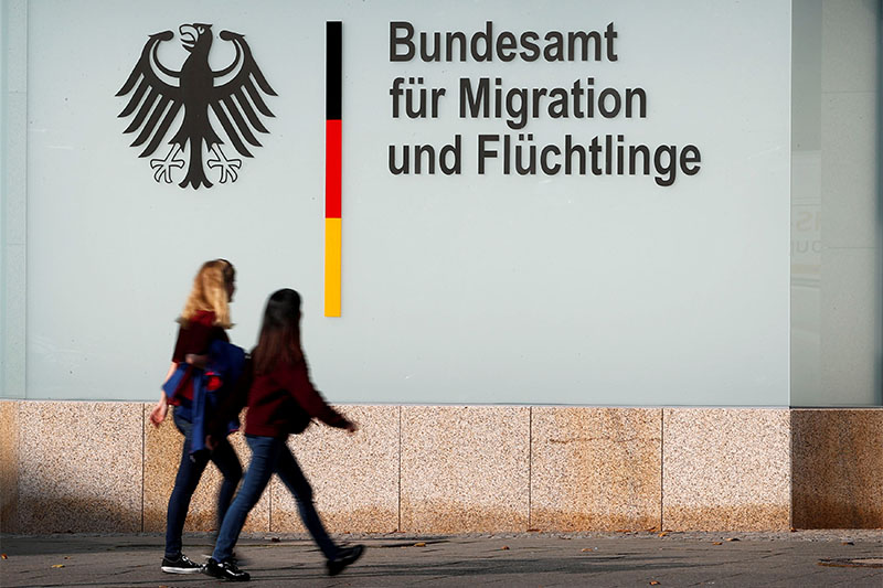 FILE PHOTO: People walk in front of an office building of the Federal Office for Migration and Refugees (BAMF) in Berlin, Germany, October 15, 2017.  Photo: Reuters