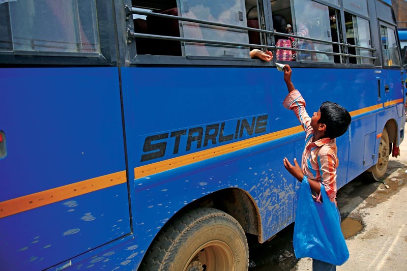 An 8-years-old boy sells mineral water to a passenger at a bus stand on World Day against Child Labor in Lalitpur, Nepal on Tuesday, June 12, 2018. Photo: THT