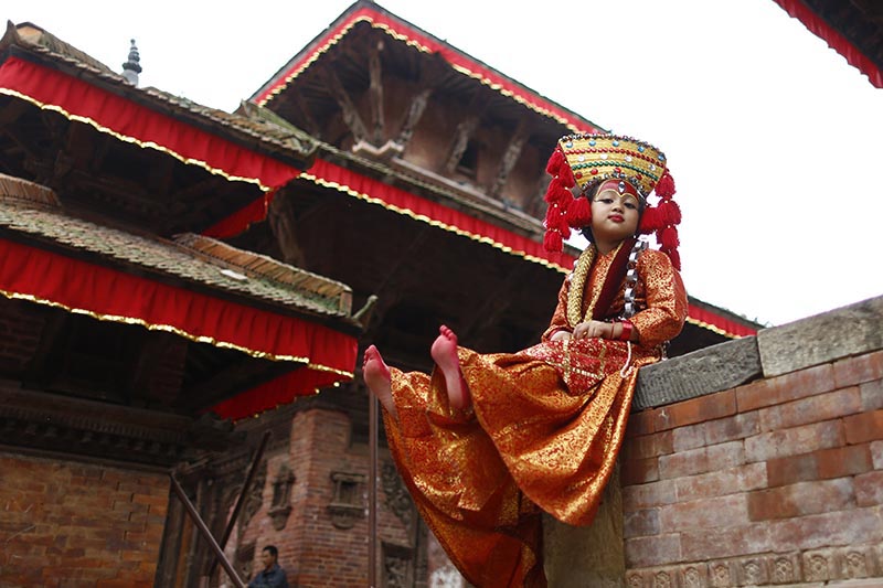 A girl adorned as 'Kumari', the 'Living Goddess' sitting on a wall  under a temple before taking part in prayer rituals, in Kathmandu Durbar Square, on Saturday, September 22, 2018. Hundreds of young girls under the age of nine gathered around the temple to offer worship for good luck, protection from evil and prevent from diseases. Photo: Skanda Gautam/THT