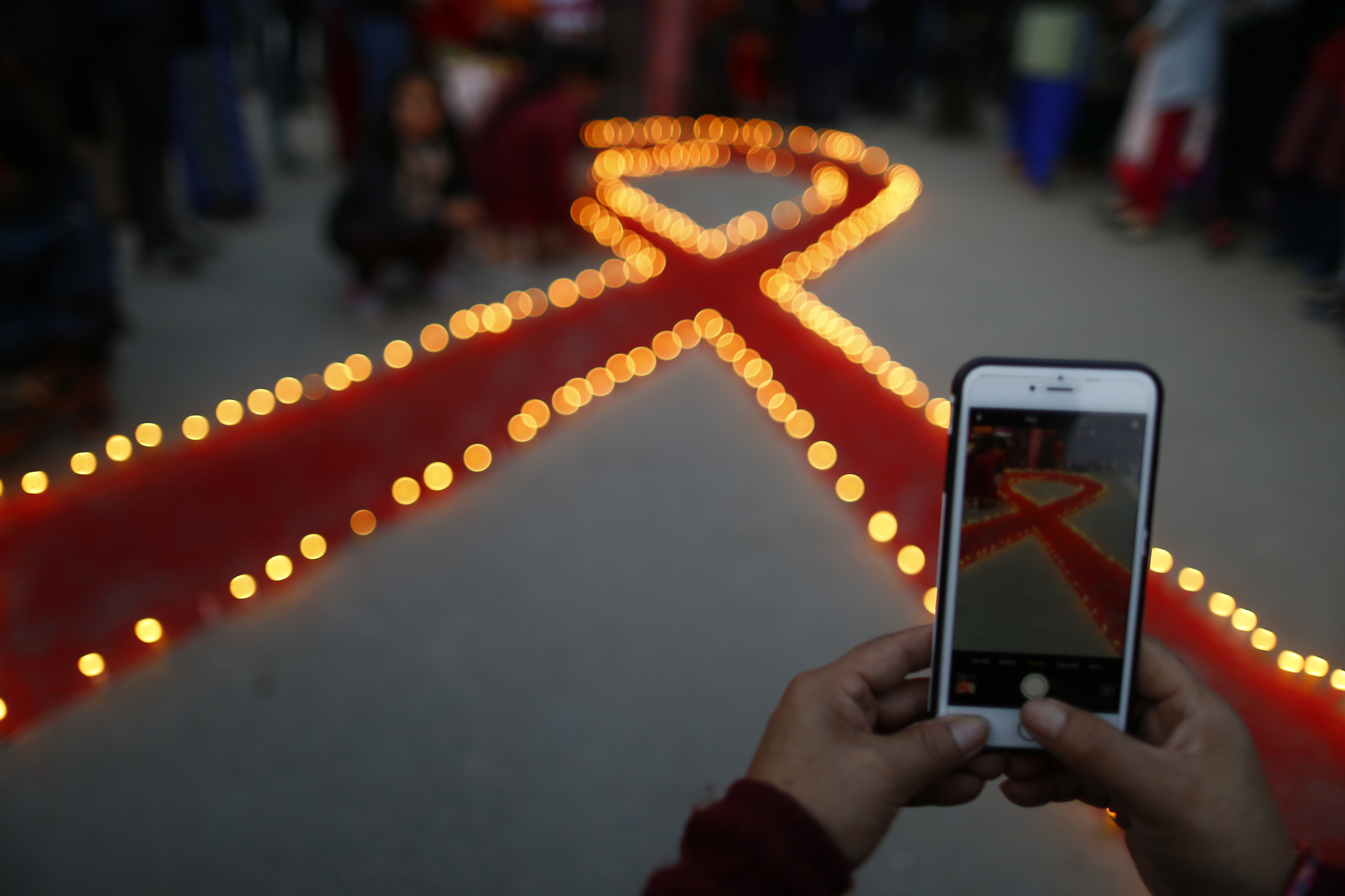 A woman takes a photo of lit candles around a red ribbon as she takes part in a candle light program commemorating and marking the 30th World Aids Day organised by Maiti Nepal in Kathmandu on Friday, November 30, 2018.