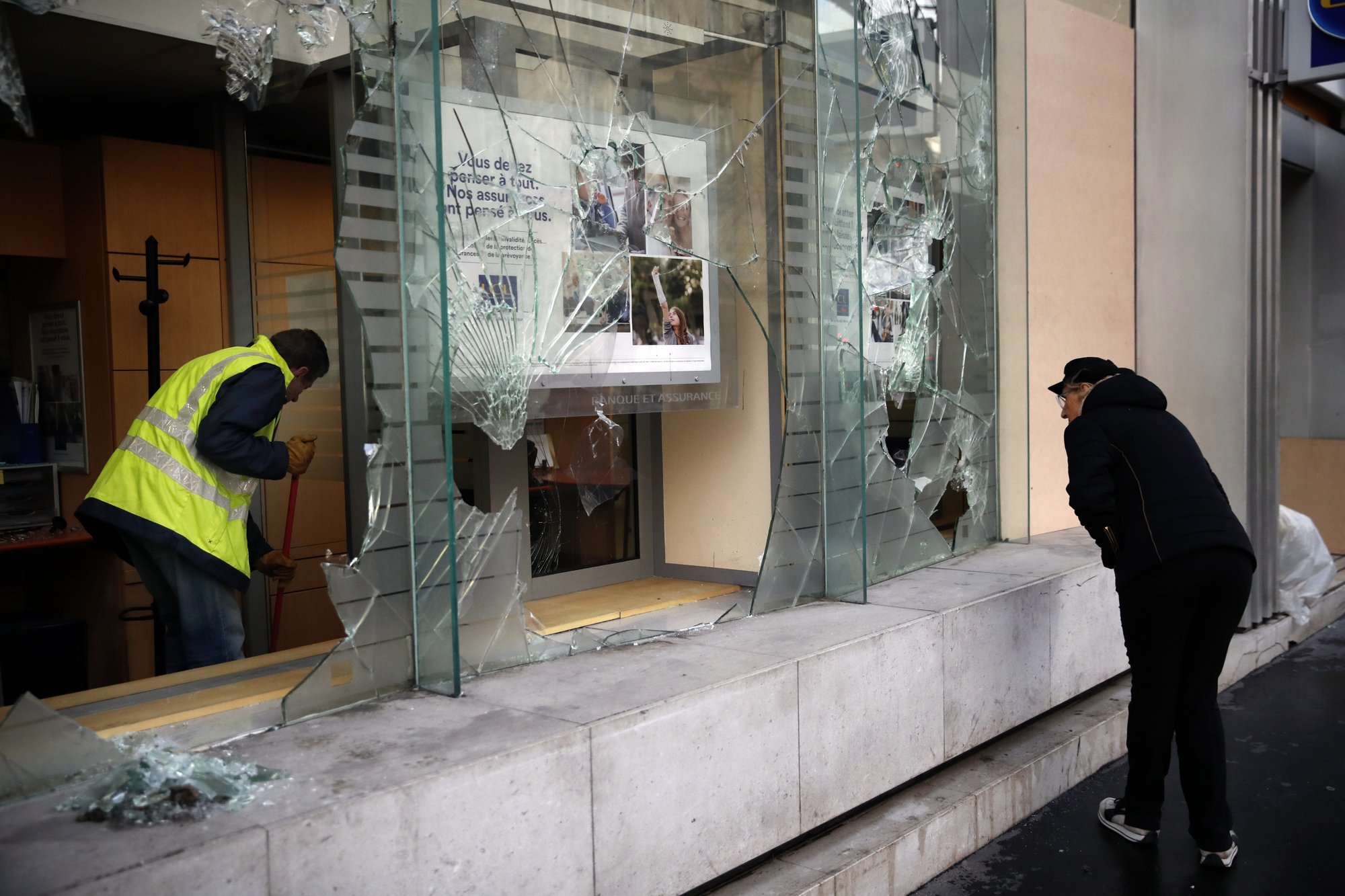 A worker clears debris in a bank as a man watches through smashed windows, in Paris, on Sunday, Dec. 9, 2018. Photo: AP