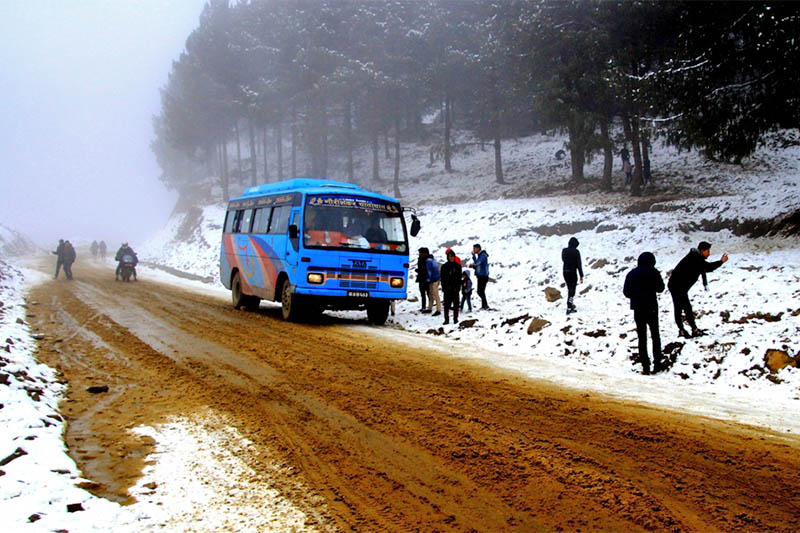 A bus awaits its passenger as they play snow along the road in Mude of Dolakha district, on Friday, January 25, 2019. Photo: Gokaran Bhandari
