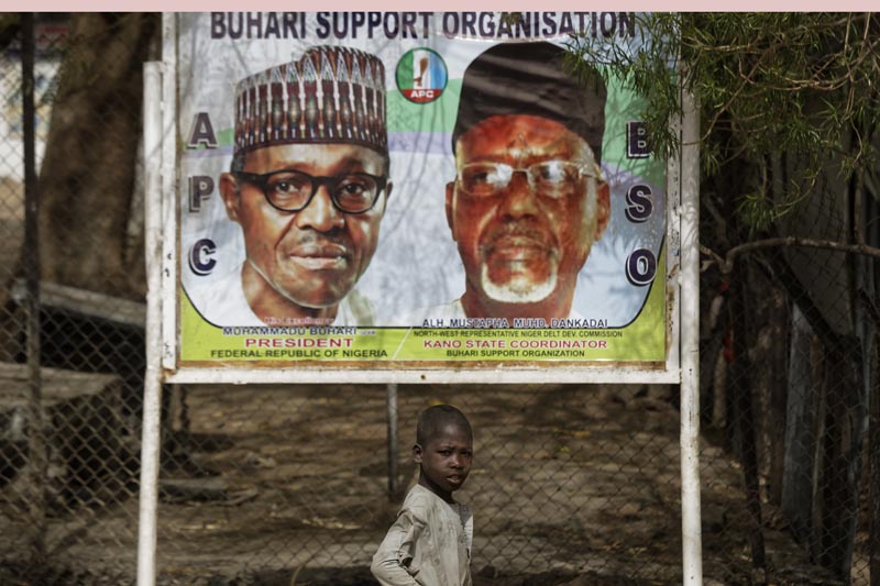 A young boy scavenges for re-sellable items from garbage on the streets, as he walks past a sign showing incumbent President Muhammadu Buhari, left, and local party official Mustapha Dankadai, right, in Kano, northern Nigeria Friday, February 15, 2019. Nigeria is due to hold general elections on Saturday, pitting incumbent President Muhammadu Buhari against leading opposition presidential candidate Atiku Abubakar. Photo: AP