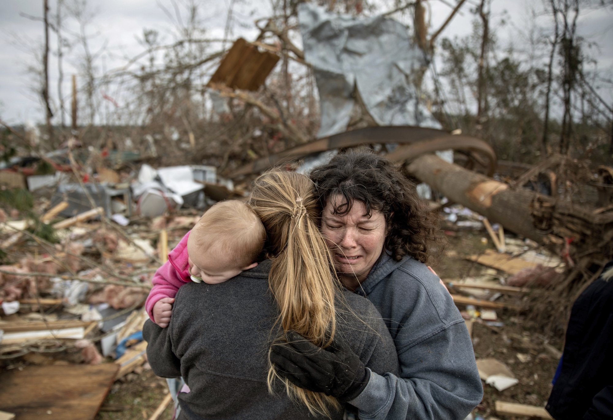 Carol Dean, right, cries while embraced by Megan Anderson and her 18-month-old daughter Madilyn, as Dean sifts through the debris of the home she shared with her husband, David Wayne Dean, who died when a tornado destroyed the house in Beauregard, Ala., on Monday, March 4, 2019. Photo: AP