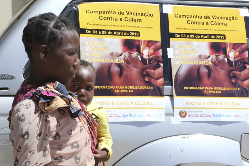 A woman and her baby walk past cholera vaccination campaign posters on the first day of the cholera vaccination programme at a camp for displaced survivors of cyclone Idai in Beira,Mozambique, Wednesday, April, 3, 2019.  Photo: AP