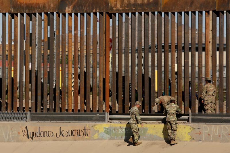 FILE: US soldiers walk next to the border fence between Mexico and the United States, as migrants are seen walking behind the fence, after crossing illegally into the US to turn themselves in, in El Paso, Texas, US, in this picture taken from Ciudad Juarez, Mexico, April 3, 2019. Photo: Reuters/file