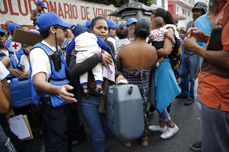 A woman with a child carries an empty container and water purification pills that came in the first aid shipment from the International Red Cross in Caracas, Venezuela, Tuesday, April 16, 2019. Photo: AP