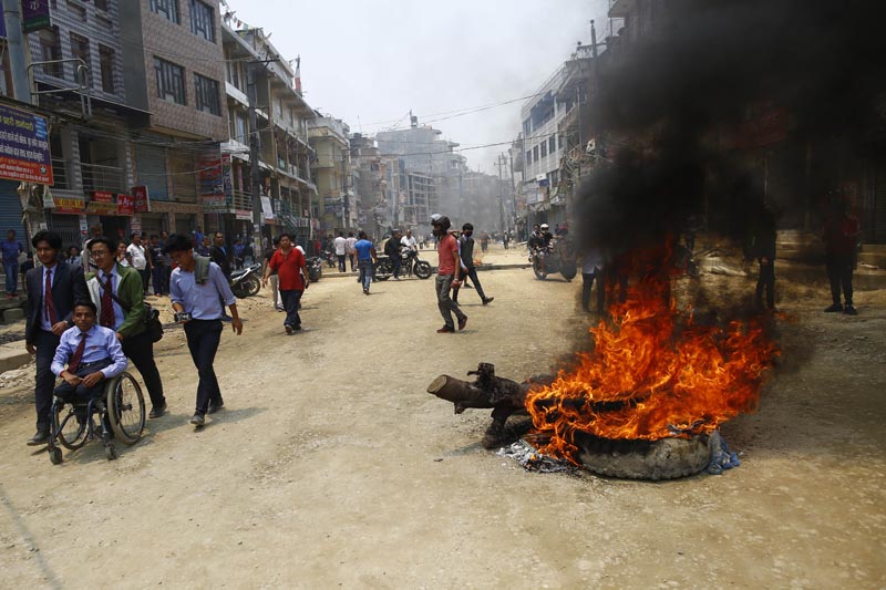 People pass by a tire in flames after local residents staged a protest against the delay in blacktopping the under-construction road, in Bouddha, Kathmandu, on Thursday, May 09, 2019. The 11.46-kilometre road expansion work has been delayed for more than four years causing high dust pollution. Photo: Skanda Guatam/THT