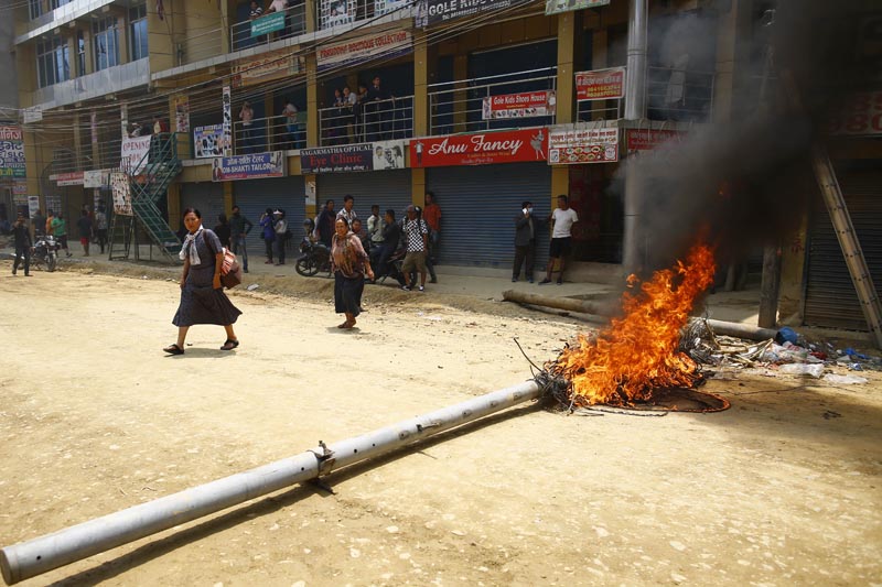 People pass by an electricity pole on fire set ablaze by local residents during a protest against the delay in blacktopping the under-construction road at Bouddha, in Kathmandu, on Thursday, May 09, 2019. Photo: Skanda Gautam/THT