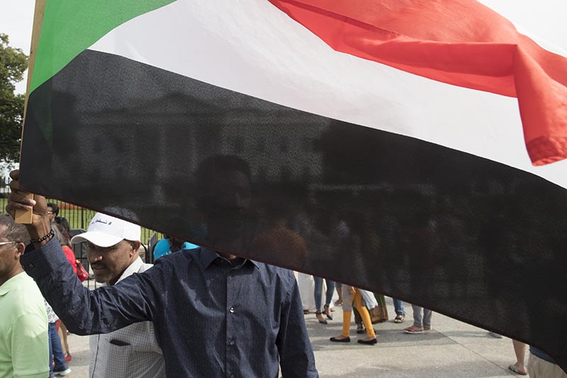 The White House is visible behind a man holding a Sudanese flag as Sudanese Americans rally outside the White House in Washington, Saturday, June 8, 2019, in solidarity with Pro-democracy protests in Sudan. Photo: AP