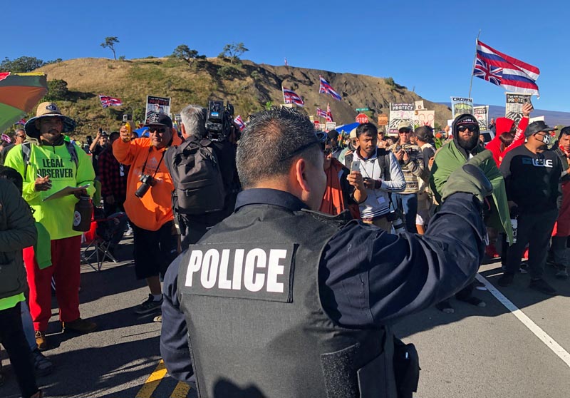 A police officer gestures at demonstrators blocking a road at the base of Hawaii's tallest mountain, Monday, July 15, 2019, in Mauna Kea, Hawaii, who are protesting the construction of a giant telescope on land that some Native Hawaiians consider sacred. Photo: AP