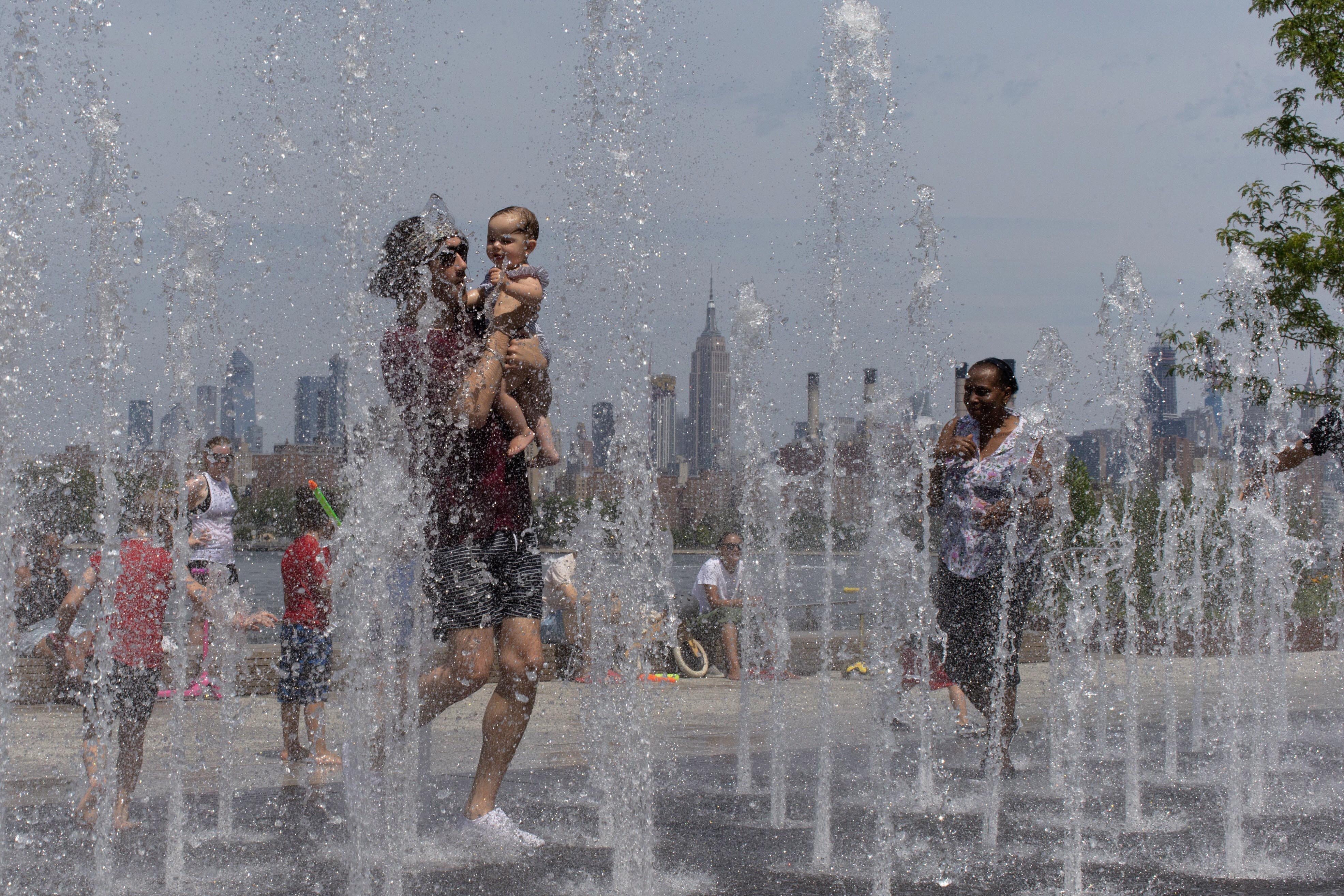 People enjoy the day playing in a water fountain as the Empire State Building is seen from Williamsburg section of Brooklyn on Saturday, July 20, 2019 in New York. Photo: AP