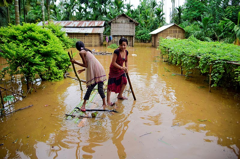 FILE PHOTO: Girls row a makeshift raft past submerged houses at a flood-affected village in Karbi Anglong district, in the northeastern state of Assam, India, July 11, 2019. Photo: Reuters
