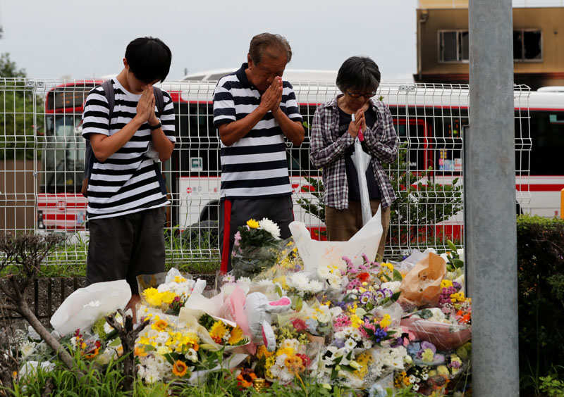 People pray in front of a row bouquets placed out for victims of the torched Kyoto Animation building in Kyoto, Japan, July 20, 2019. Photo: Reuters