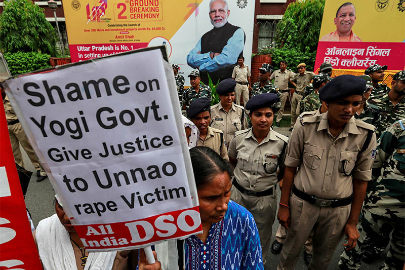 The images of India's Prime Minister Narendra Modi and Uttar Pradesh Chief Minister Yogi Adityanath are seen on hoardings as an activist holds a placard during a protest demanding investigation in a highway collision in which a woman who is fighting a rape case against a legislator of the ruling Bharatiya Janata Party (BJP) was critically injured, in New Delhi, India, July 30, 2019. Photo: Reuters