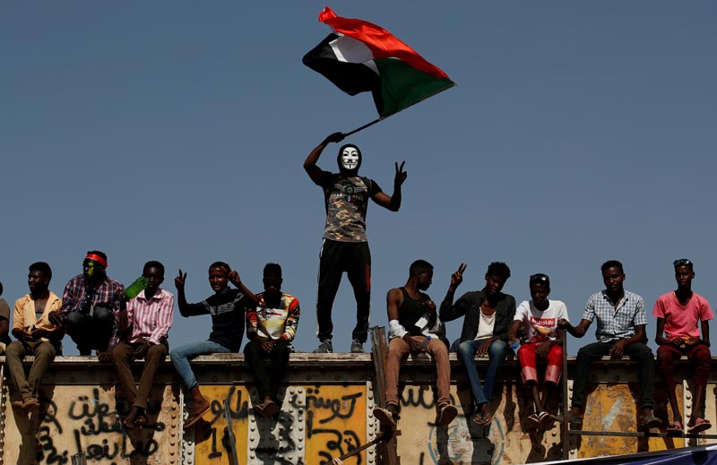 FILE: A Sudanese protester wearing a Guy Fawkes mask waves a national flag outside the Defense Ministry compound in Khartoum, Sudan, April 24, 2019. Photo: Reuters