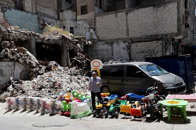 FILE PHOTO: A street vendor sells toys next to rubble of damaged buildings in the city of Idlib, Syria May 25, 2019. Photo: Reuters