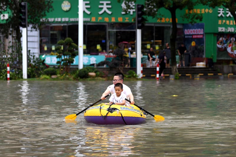A man rows an inflatable kayak carrying a boy on a flooded street after Typhoon Lekima hit Wenling, Zhejiang province, China August 10, 2019. Picture taken August 10, 2019. REUTERS/Stringer ATTENTION EDITORS - THIS IMAGE WAS PROVIDED BY A THIRD PARTY. CHINA OUT.