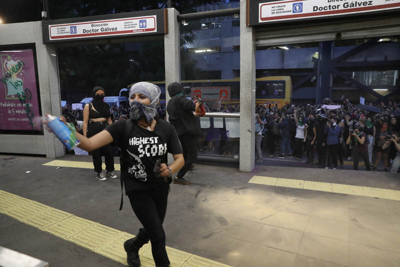 A masked protester spray paints a bus station during a women's protest march sparked by a string of alleged sexual attacks by police officers, in Mexico City, Friday, August 16, 2019.  Photo: AP