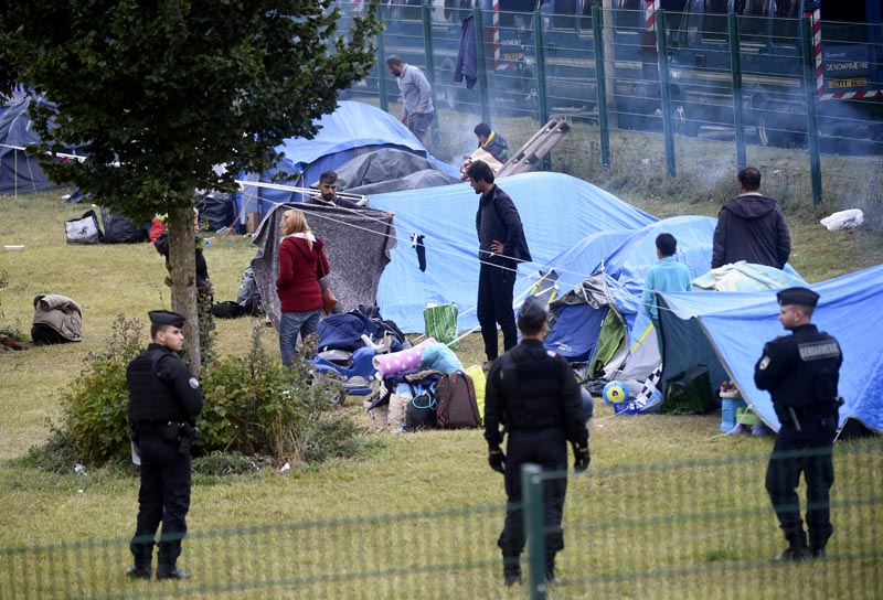 French police officers watch migrants packing their belongings in a camp of Grande Synthe, northern France, Tuesday, Sept 17, 2019. Photo: AP