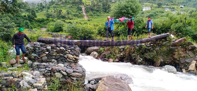 People crossing the river using wooden log while carrying a patient to a health facility, in Bajura district. Photo: Prakash Singh/THT