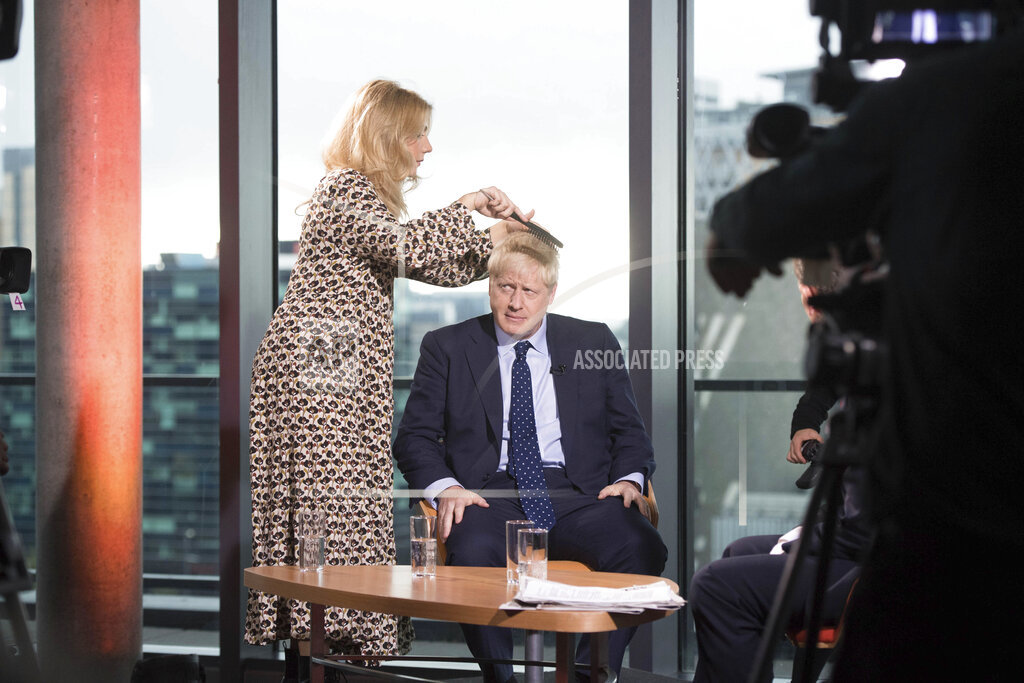 British Prime Minister Boris Johnson has his hair combed as he prepares to appear on a TV political show at Media City in Salford, England before opening the Conservative party annual conference Sunday Sept. 29, 2019.  Johnson headed Sunday to the Conservative Party conference in Manchester, where the party is widely expected to endorse government plans to spend more on the country's National Health Service. (Stefan Rousseau/PA via AP)