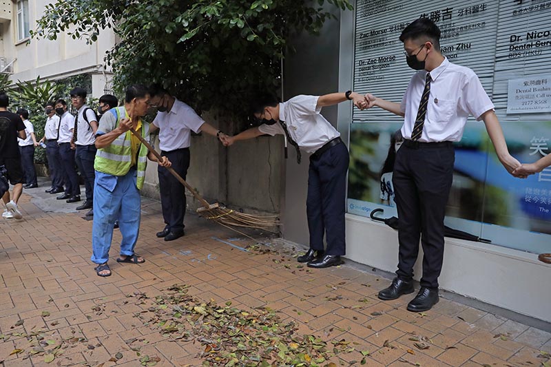 A worker sweeps a road as students hold hands to surround St. Paul's College in Hong Kong, Monday, on September 9, 2019. Photo: AP