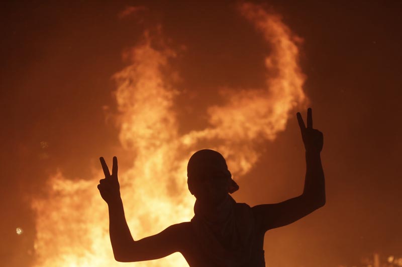 An anti-government protester makes victory signs in front a fire set to block a road during a demonstration in Beirut, Lebanon, Thursday, October 17, 2019. Photo: AP