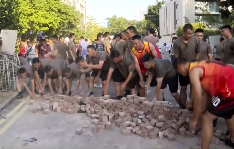 In this image made from video, Peopleu0092s Liberation Army soldiers, dressed in shorts and T-shirts pick up bricks scattered by protesters at Hong Kong Baptist University in Hong Kong, Saturday, Nov 16, 2019. Photo: Television Broadcasts Limited Hong Kong via AP