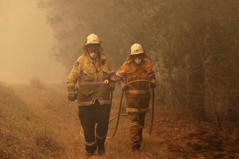 Firefighters drag their water hose after putting out a spot fire near Moruya, Australia, Saturday, Jan. 4, 2020. Photo: AP